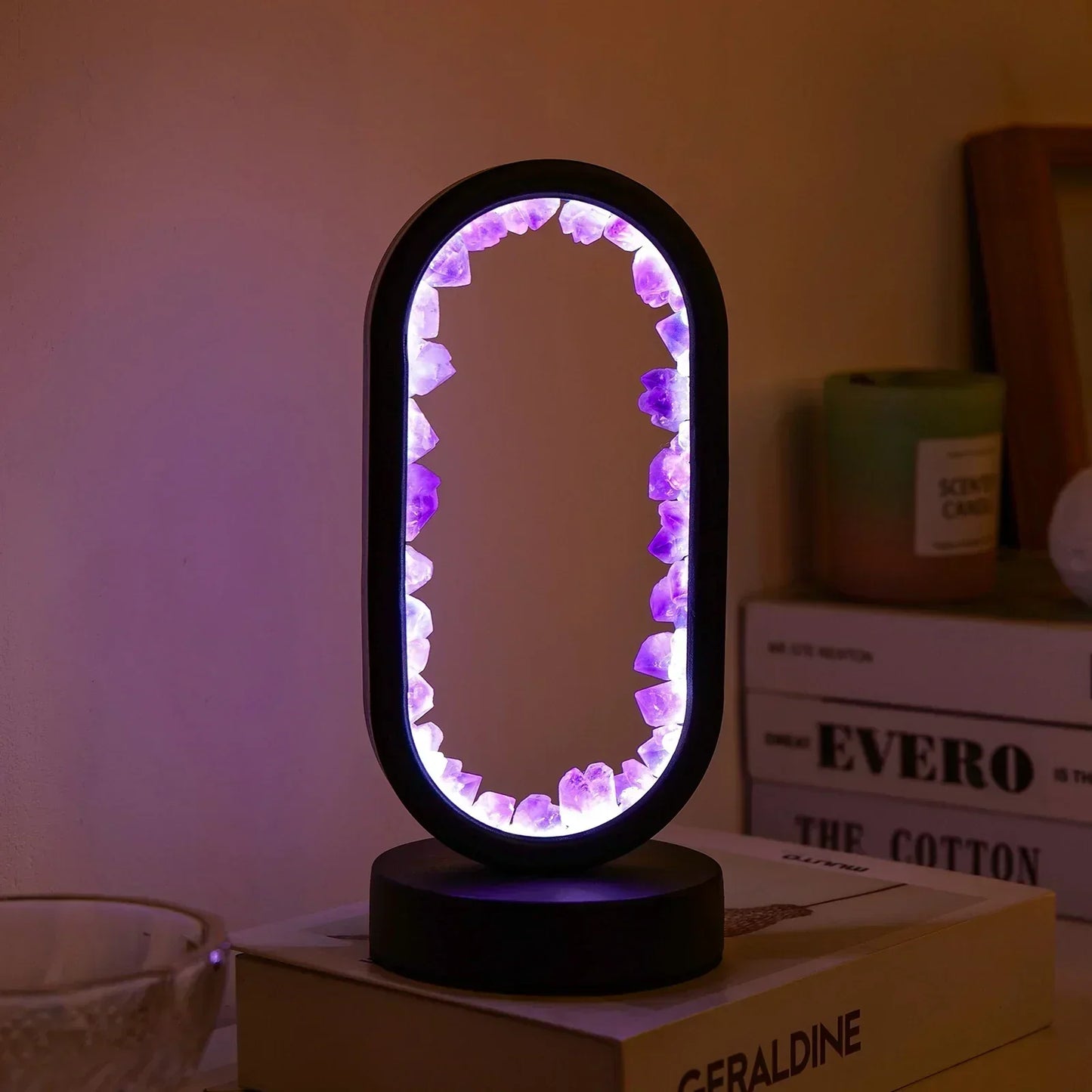 Fitlybuy AuraStone lamp with a black oval frame lined with glowing purple amethyst crystals on a book-filled desk.