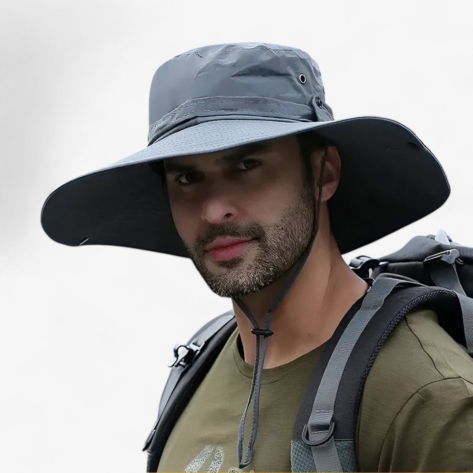 Man wearing a grey, wide-brimmed Fitlybuy Zeno UV sun hat with a chin strap and backpack for outdoor hiking.
