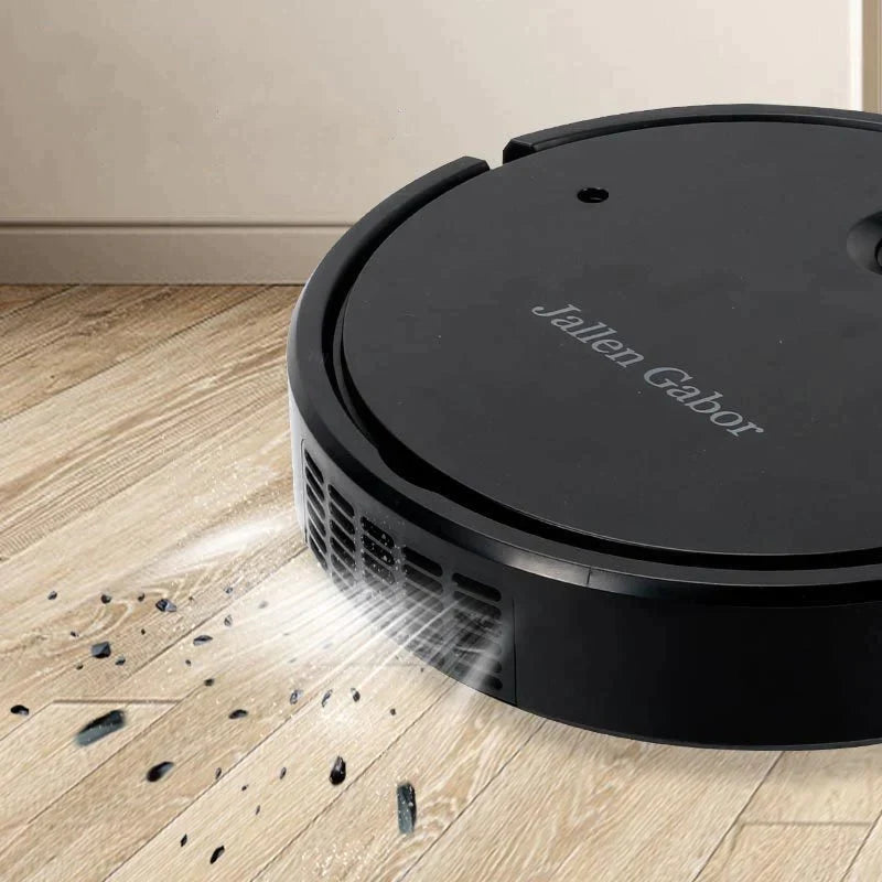 Black Fitlybuy AutoSweep robot vacuum cleaning debris from a light wood floor.