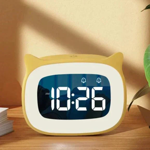 Yellow cat-shaped LED alarm clock on a wooden desk showing 10:26 AM with dual alarm indicators.