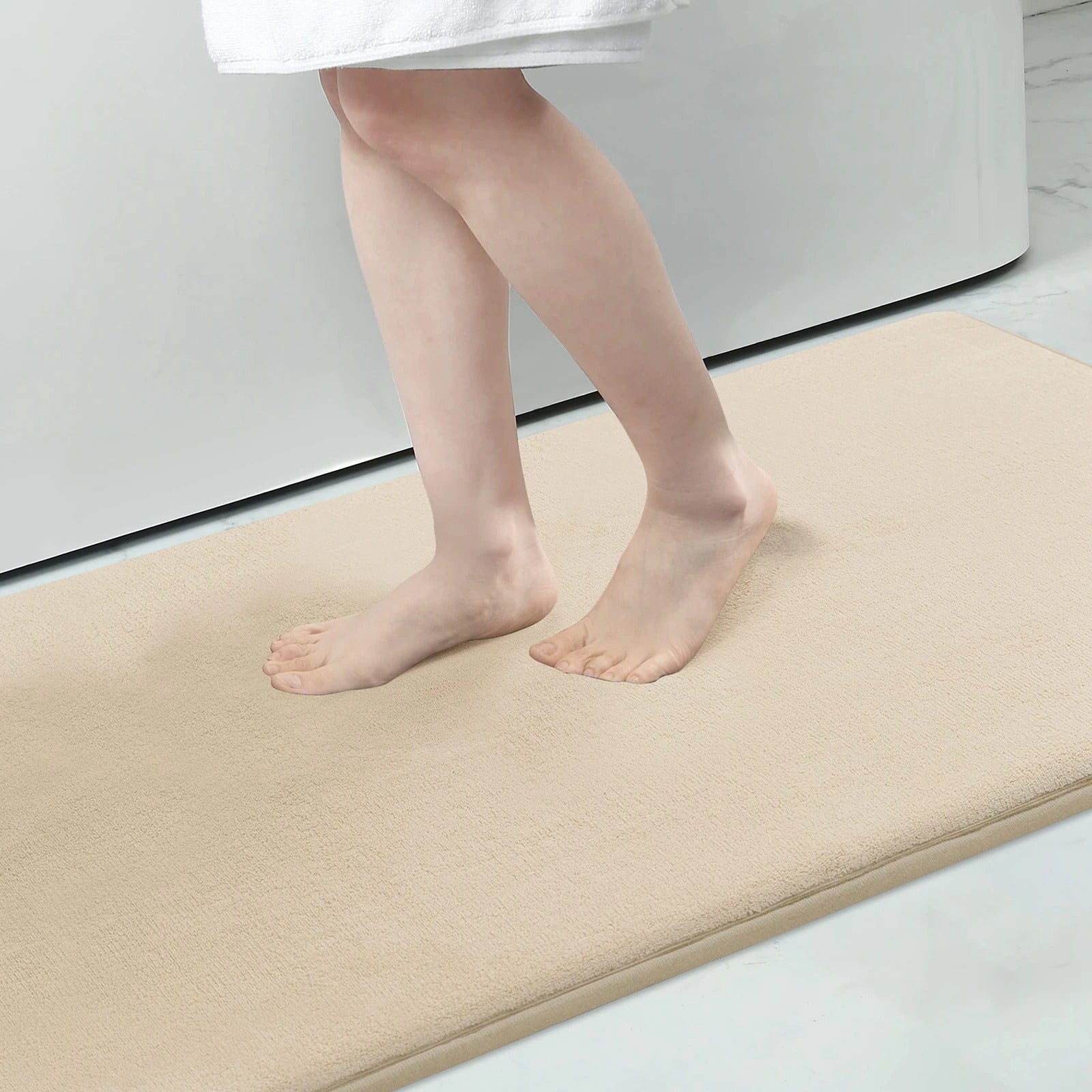 Bare feet stepping onto a plush, beige Fitlybuy memory foam bath mat in a bathroom.