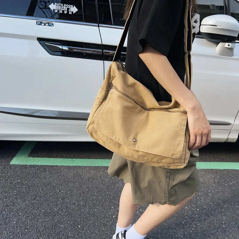 Fitlybuy canvas messenger sling bag in beige, worn over the shoulder outdoors beside a white car.