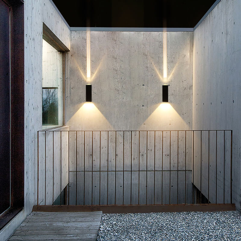 Two modern black rectangular LED wall lights mounted on a concrete wall, casting upward and downward warm light beams.