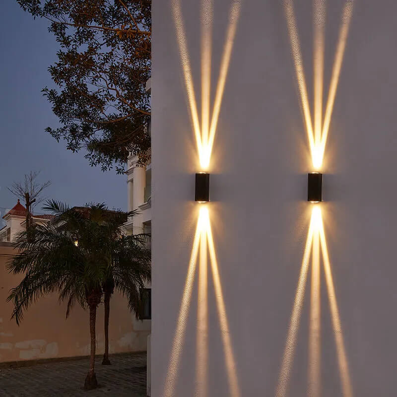 Two modern, black rectangular LED wall lights mounted outdoors, projecting dramatic upward and downward beams of light.