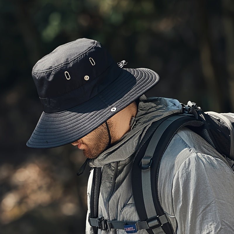 A hiker wears a black Fitlybuy SUNSAFE breathable sun hat with a wide brim and vents in a natural outdoor setting.