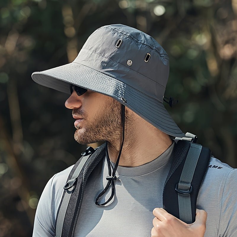 Man wearing a grey, wide-brimmed Fitlybuy SUNSAFE hiking hat with chin strap and vents in an outdoor setting.