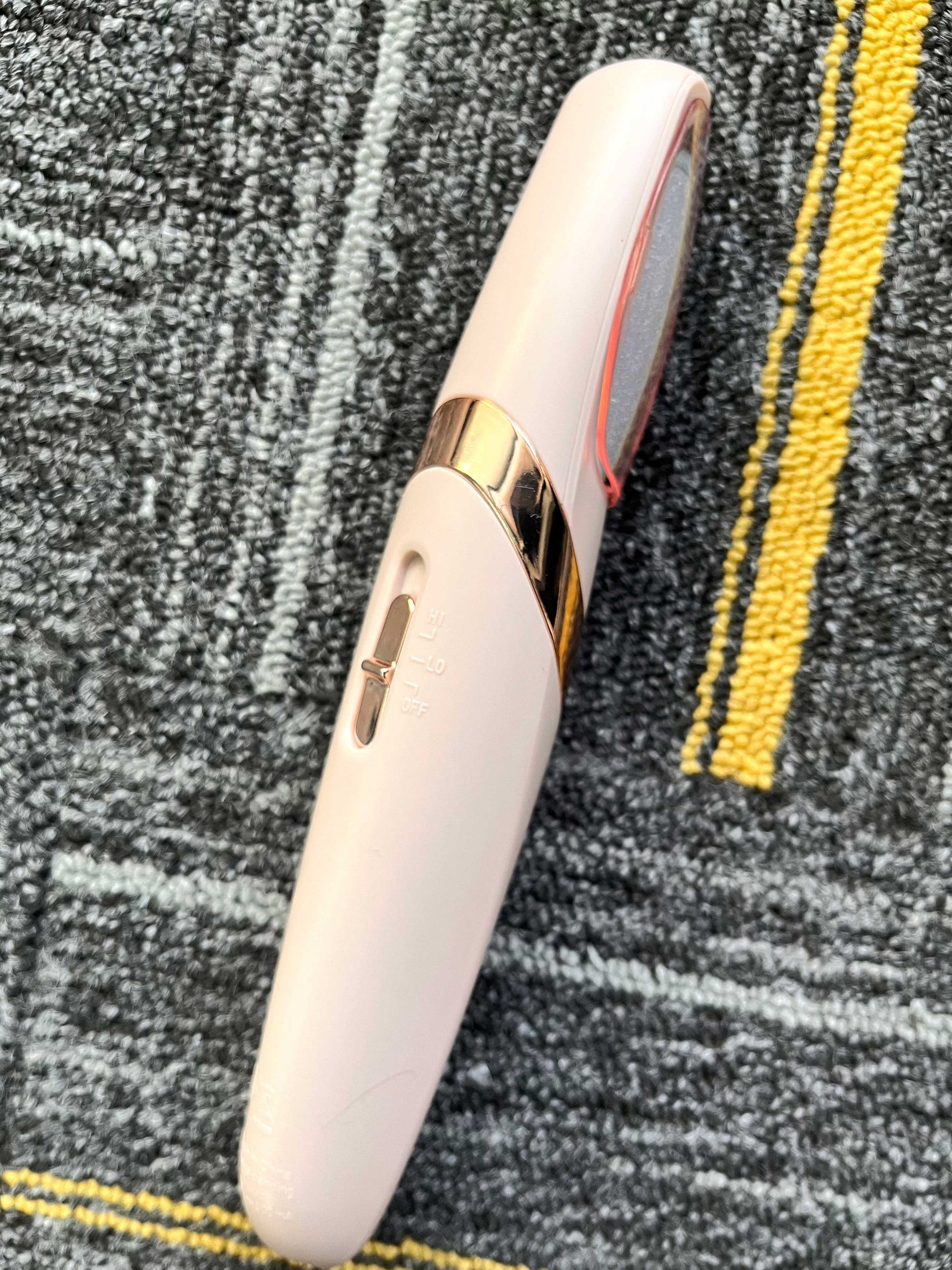 Fitlybuy electric foot grinder in pale pink with rose gold trim and Hi/Lo speed settings on a textured grey carpet.