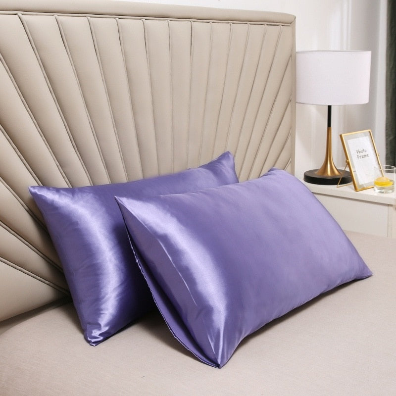 Two smooth, purple Fitlybuy satin pillowcases resting on a beige bed in front of a modern tufted headboard.