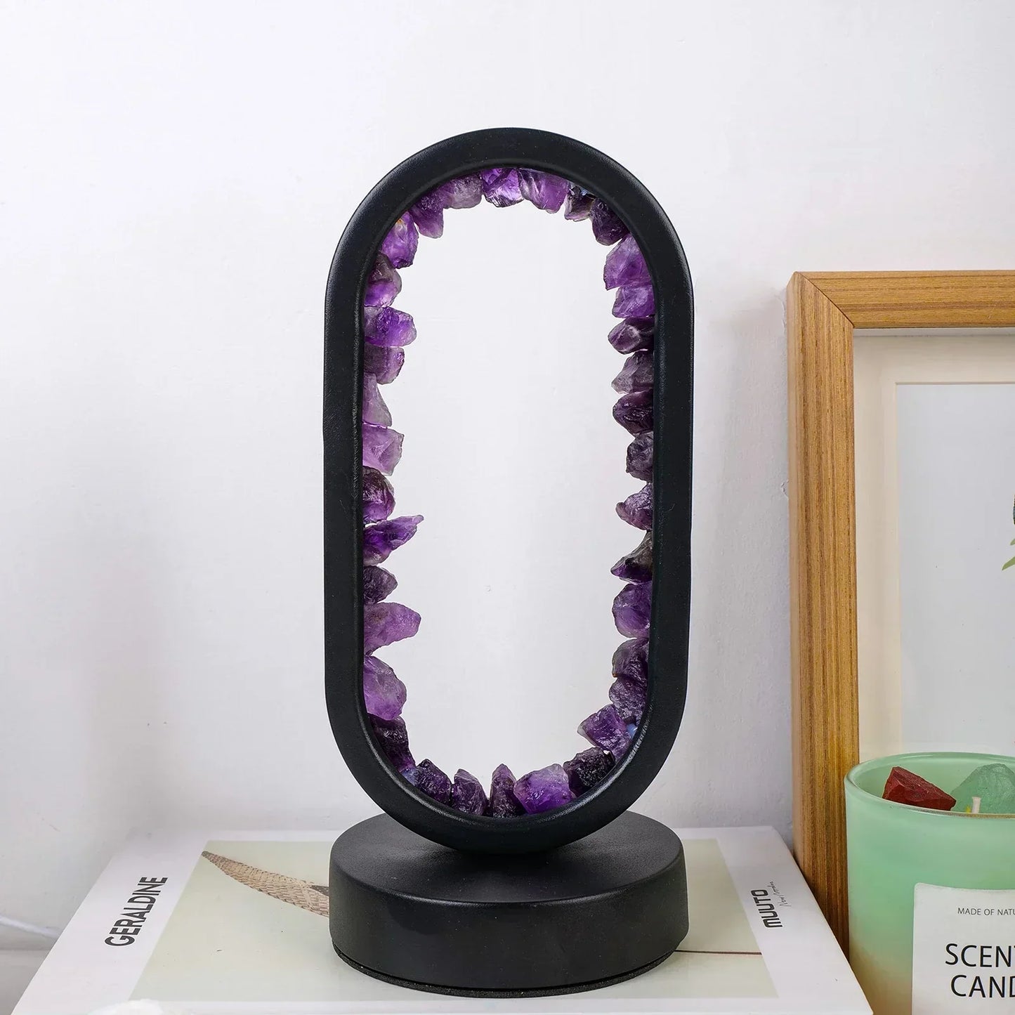 Fitlybuy AuraStone oval lamp with raw purple amethyst crystals set in a black frame on a base, sitting on a book.