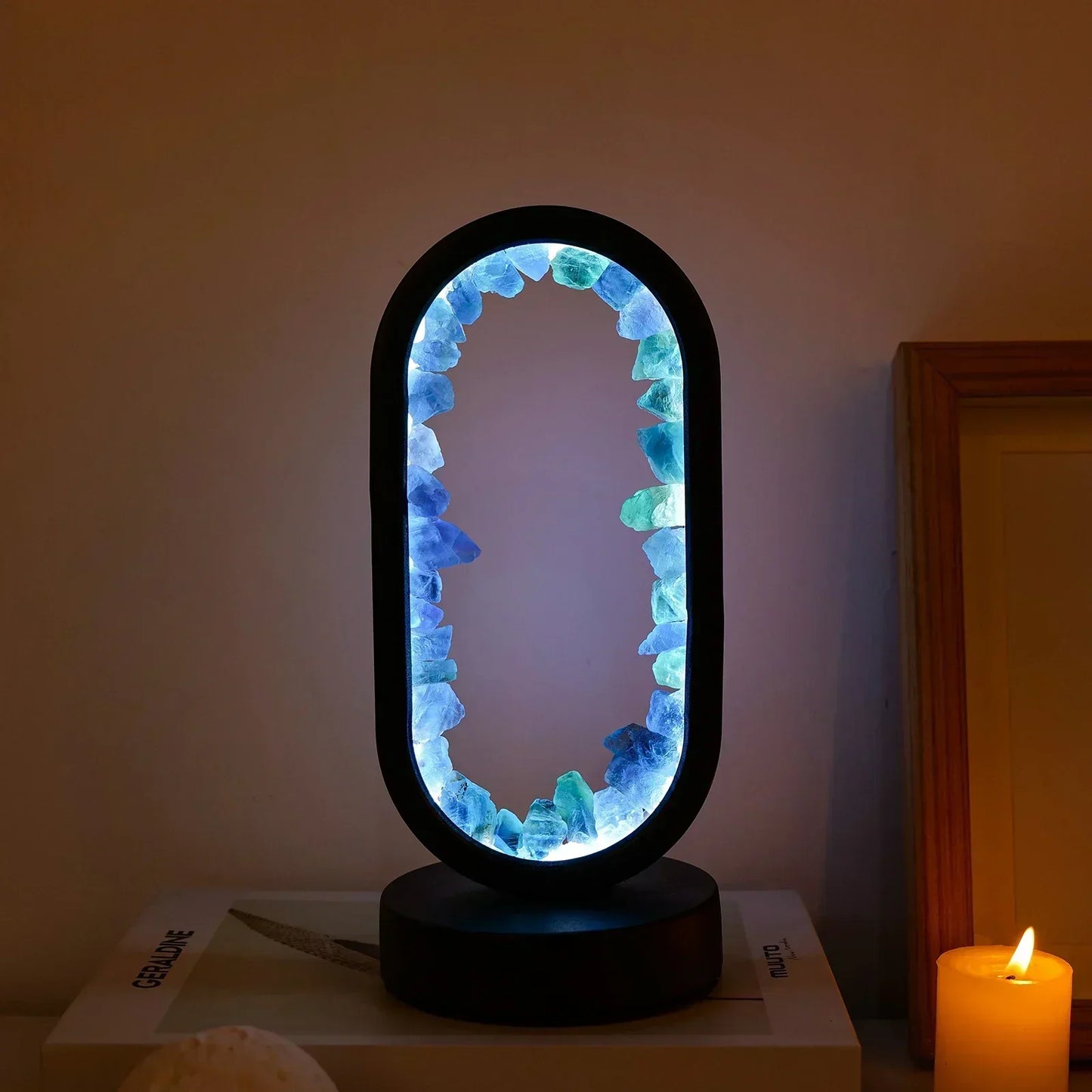 Fitlybuy AuraStone oval lamp with glowing blue and green natural crystals, on a black base next to a lit candle.