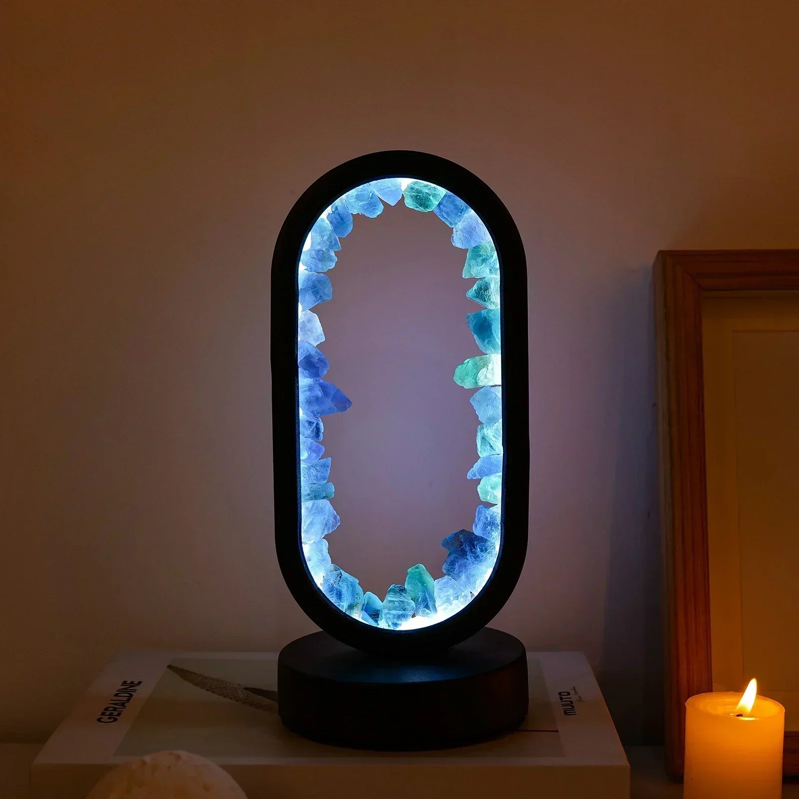 Fitlybuy AuraStone oval lamp with glowing blue and green natural crystals, on a black base next to a lit candle.