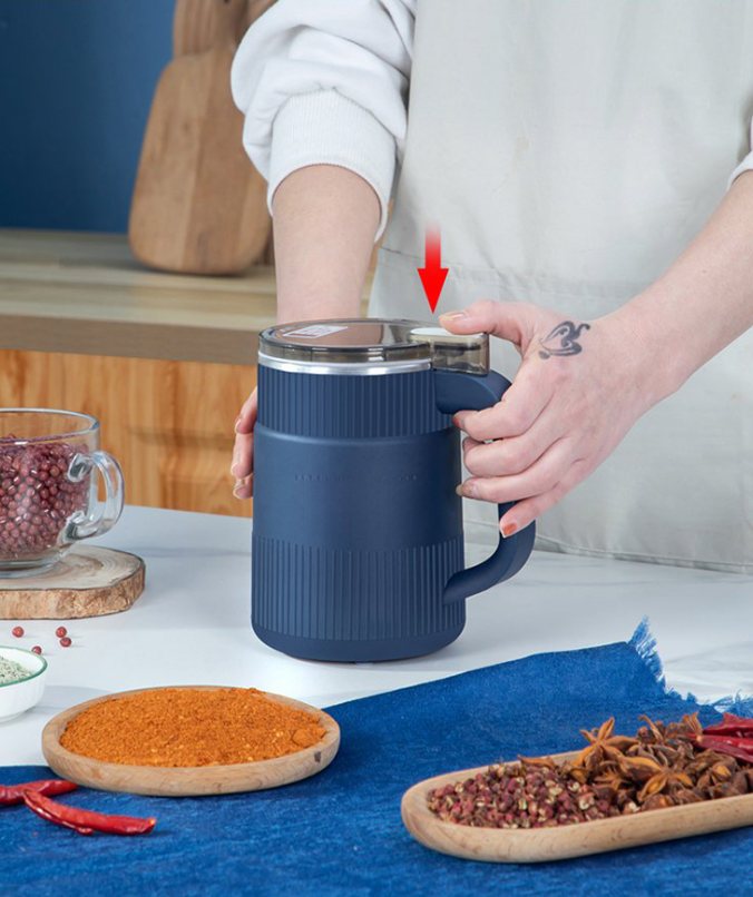 Fitlybuy navy blue electric grain mill with clear lid, being held on a kitchen table with spices and red chili peppers.