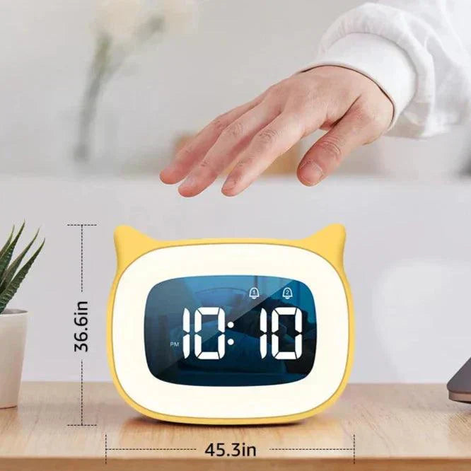 Yellow cat-shaped LED alarm clock on a desk with a hand hovering above it, showing 10:10 digital time display.