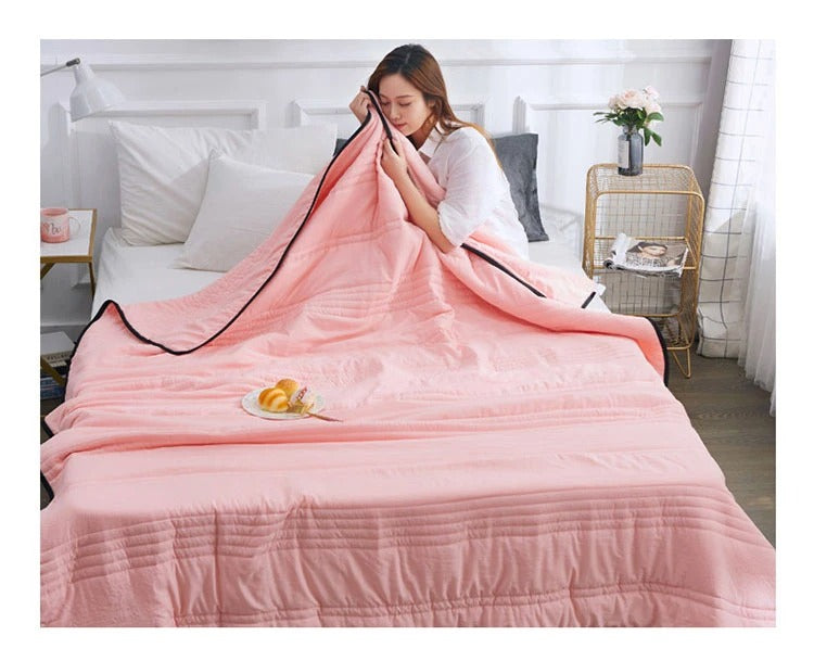 Woman on a bed holding a soft, quilted light pink Fitlybuy premium cooling blanket with black trim.