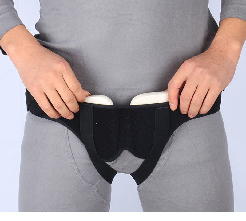 Fitlybuy black adjustable hernia support belt with white compression pads worn over grey base layer clothing.