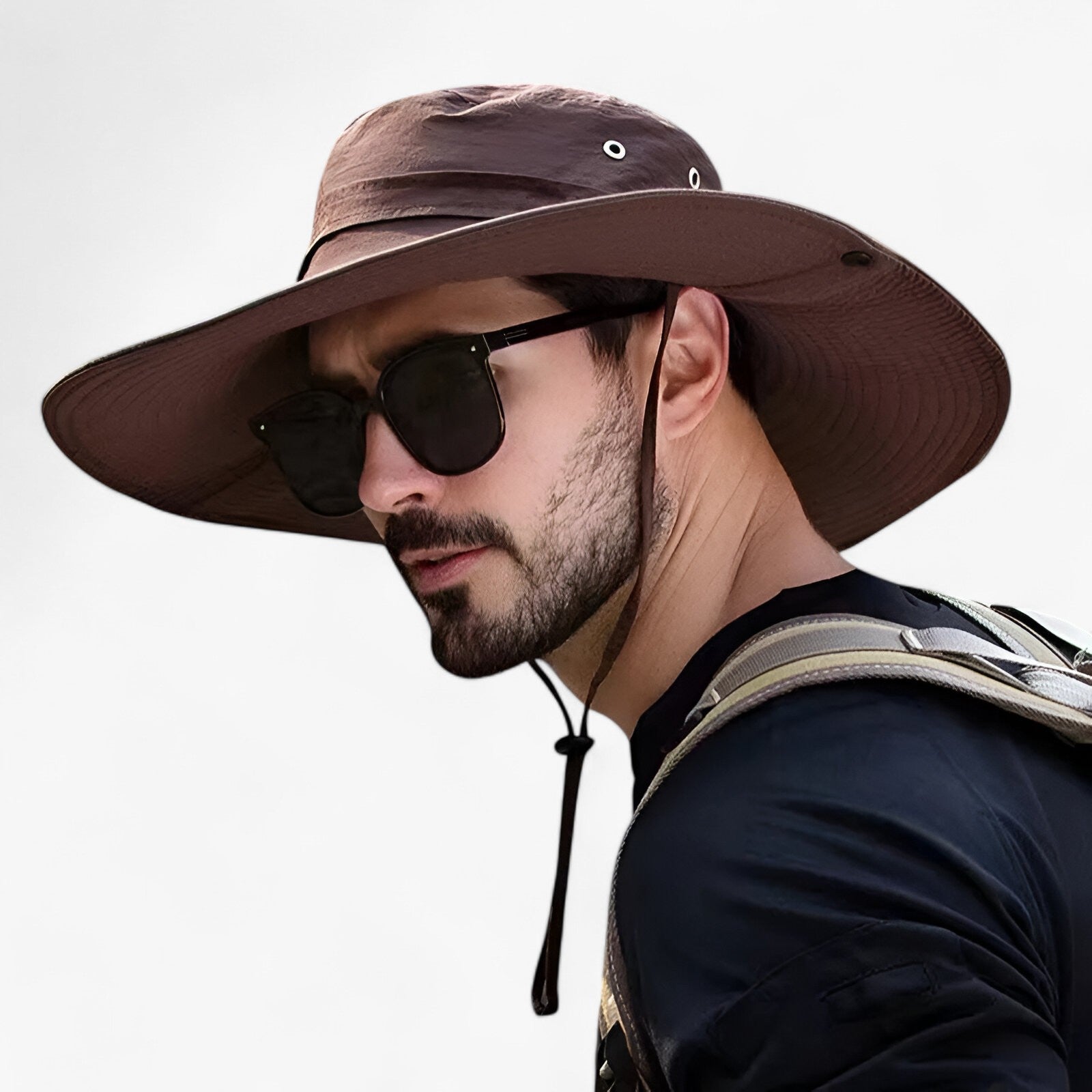 Man wearing a wide-brimmed brown Fitlybuy Zeno UV protection outdoor hat with a chin strap and breathable side vents.
