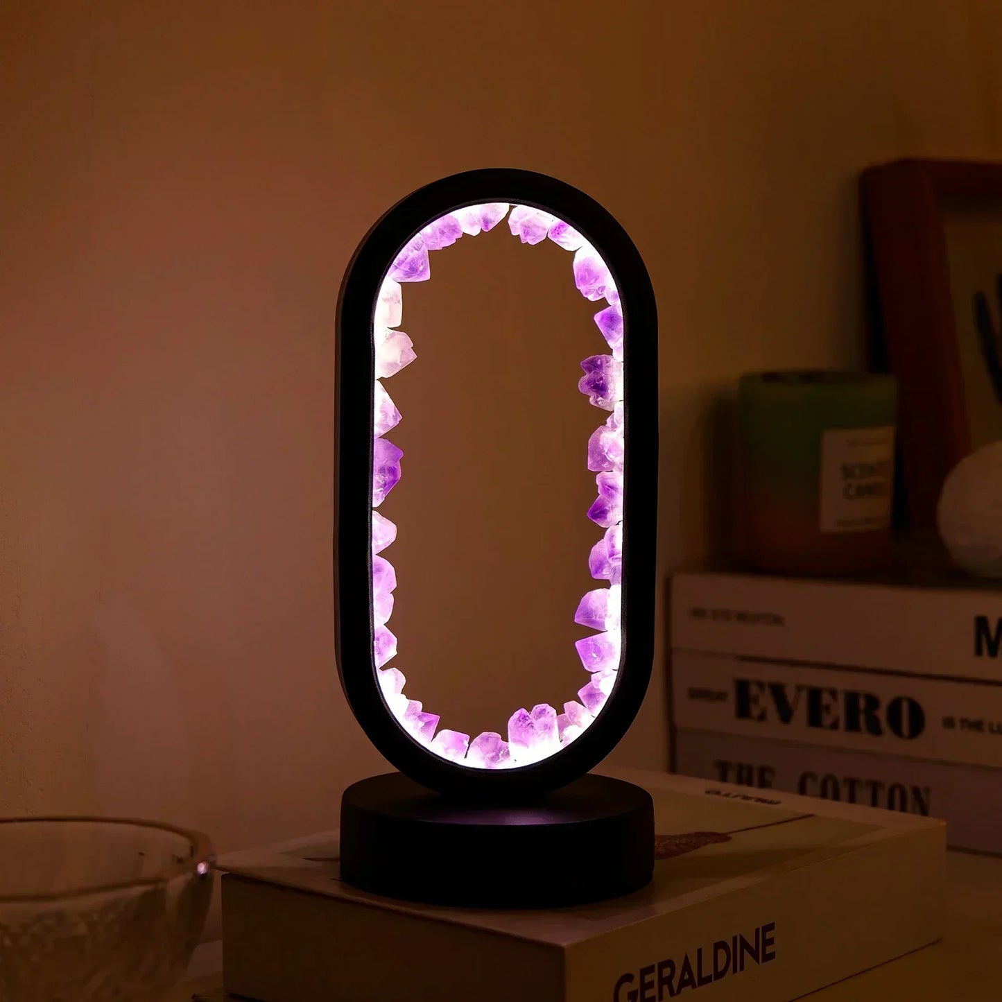 Fitlybuy AuraStone amethyst lamp with glowing purple crystal border in a black oval frame on a table with books.