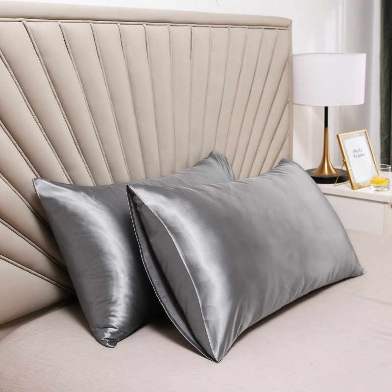 Two glossy gray Fitlybuy satin pillowcases with SoftTouch fabric on a beige bed against a modern headboard.