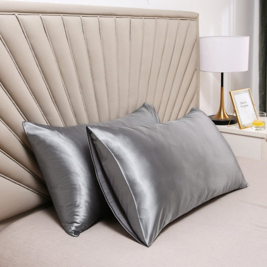 Two glossy gray Fitlybuy satin pillowcases with SoftTouch fabric on a beige bed against a modern headboard.