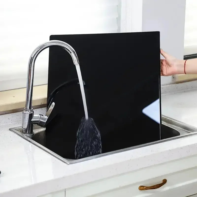 Fitlybuy black acrylic cutting board being rinsed in a kitchen sink, highlighting its hygienic and easy-clean design.