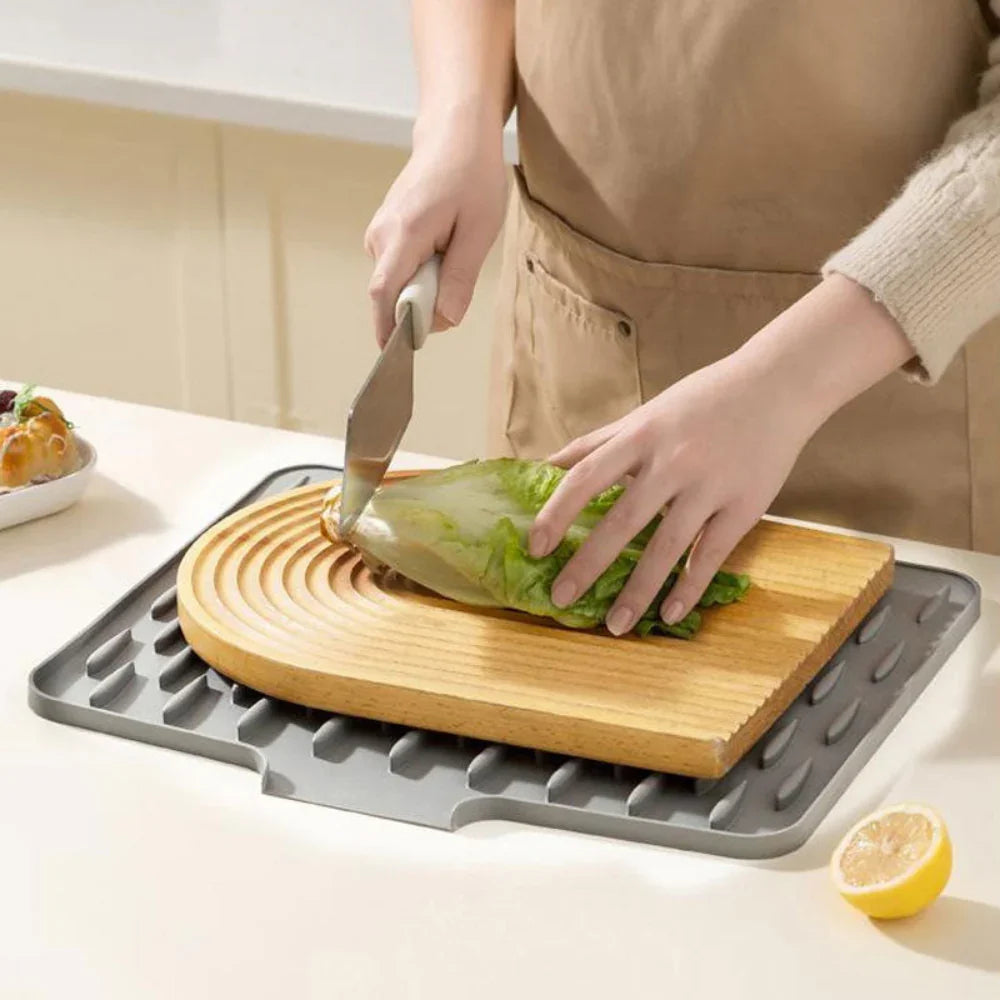 Grey Silicool silicone drying mat under a wooden cutting board with sliced lettuce, on a kitchen counter.
