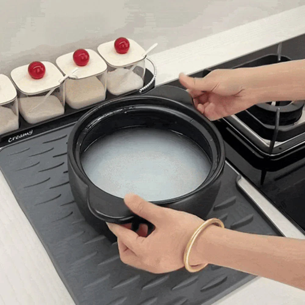Black Fitlybuy Silicool drying mat with non-slip ridges, placed on a kitchen counter under a pot and spice jars.