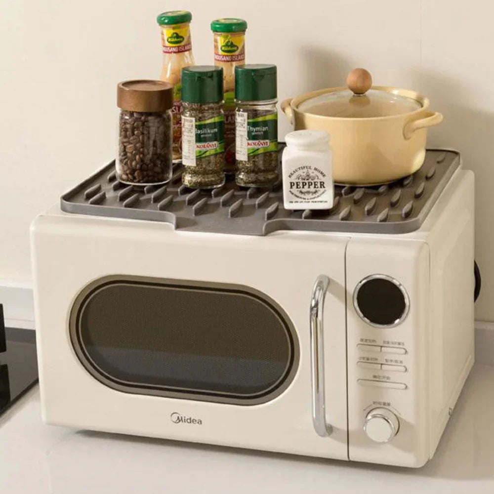 Grey Silicool silicone drying mat on a microwave, featuring heat-resistant, non-slip ridges holding kitchen jars.