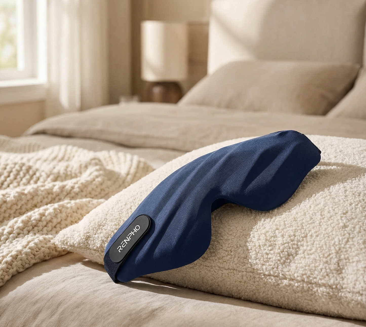 Navy blue Fitlybuy EyeSnooze Lite memory foam sleep mask resting on a cozy bedroom pillow.