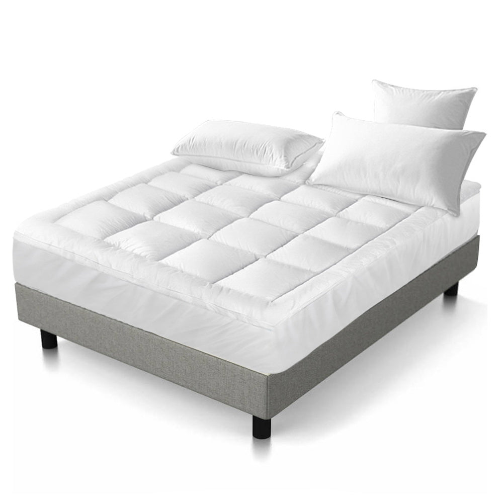White, quilted Fitlybuy luxury pillowtop mattress topper on a bed with two pillows against a plain white background.