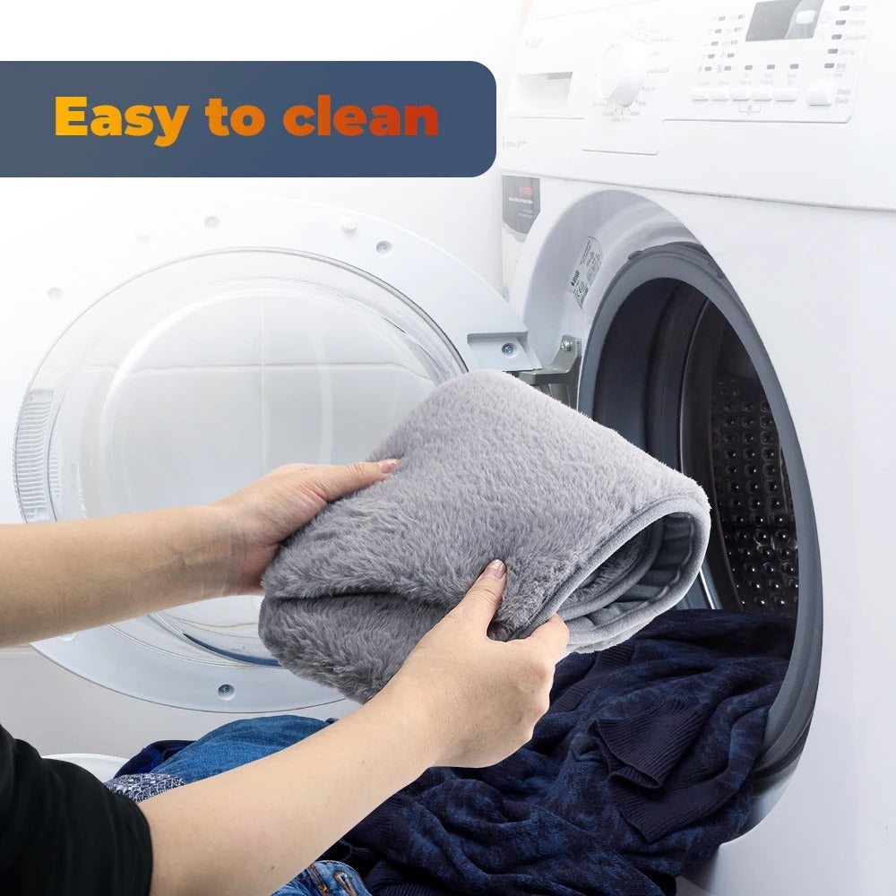 Hands placing a plush grey Fitlybuy USB electric hand/waist warmer into a washing machine. Text says "Easy to clean."