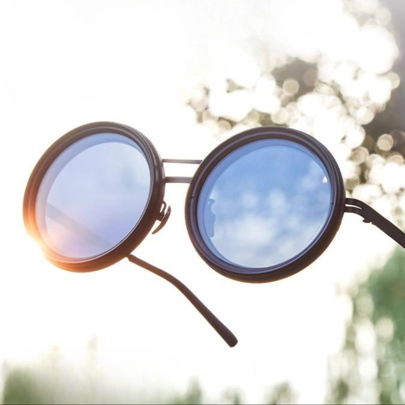 Fitlybuy round polarized sunglasses with a black metal frame held against a bright, sunny outdoor background.