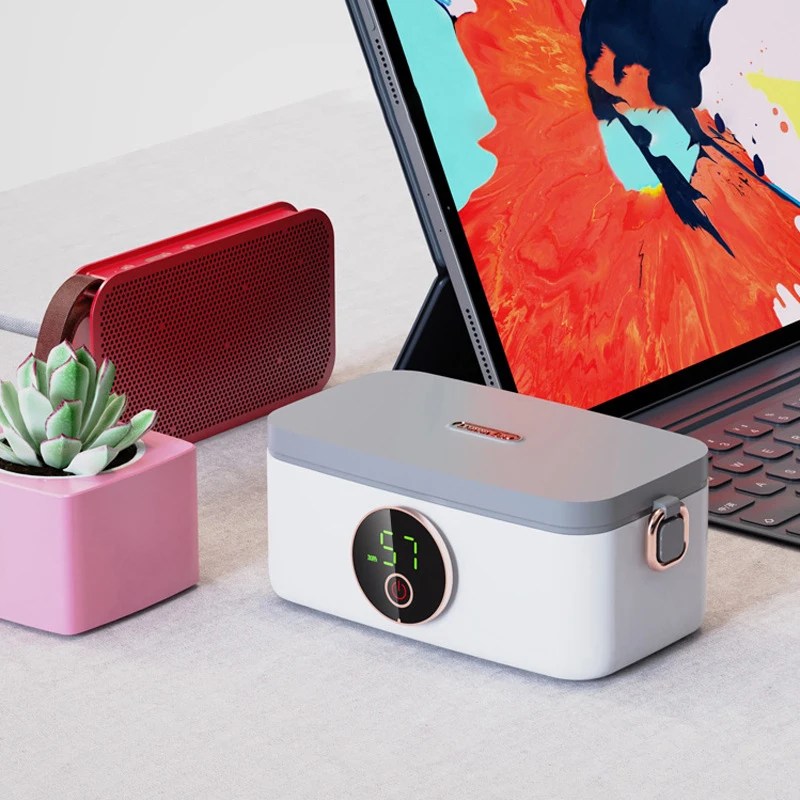Fitlybuy HeatMate Pro: A white and grey portable heated lunchbox with a digital temp display on a desk near a tablet.