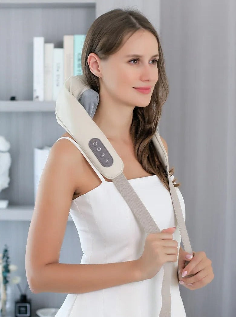 Woman wearing a beige Fitlybuy electric neck and back massager with heat therapy control panel, indoors near bookshelves.
