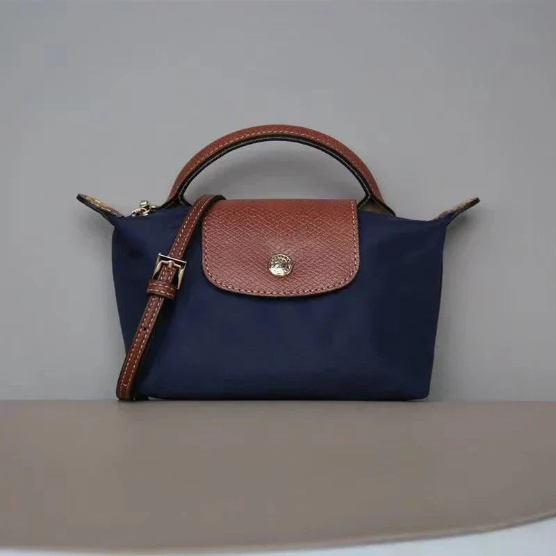 Fitlybuy Calo mini navy handbag with brown leather flap, top handle, and adjustable shoulder strap against a gray wall.