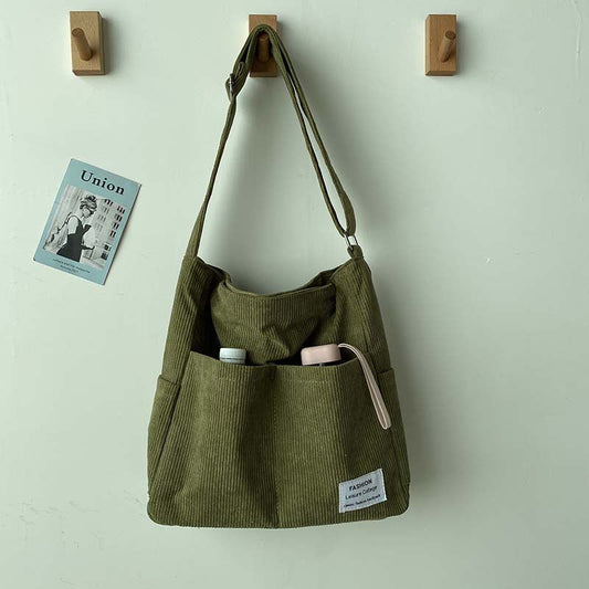 Fitlybuy olive green corduroy crossbody bag with dual front pockets, hanging on a wall hook.