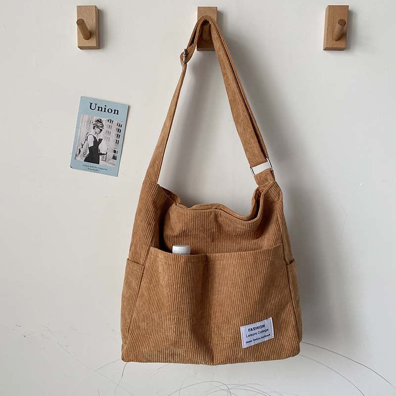Fitlybuy tan corduroy crossbody bag with adjustable strap and front pockets, hanging on a wall hook.