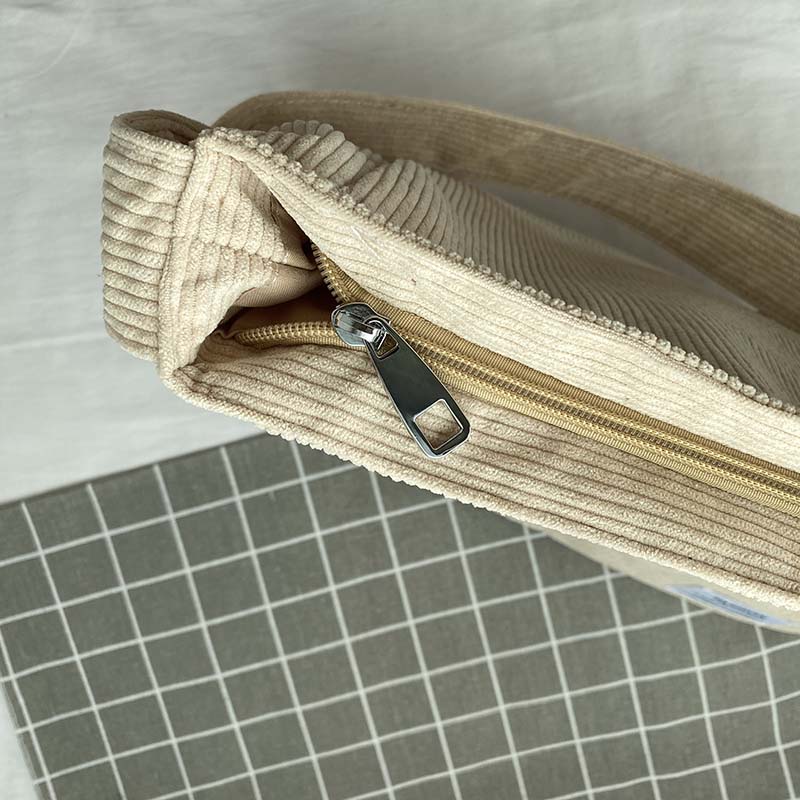 Fitlybuy cream-colored corduroy crossbody bag with a sturdy zipper closure, resting on a gray grid surface.