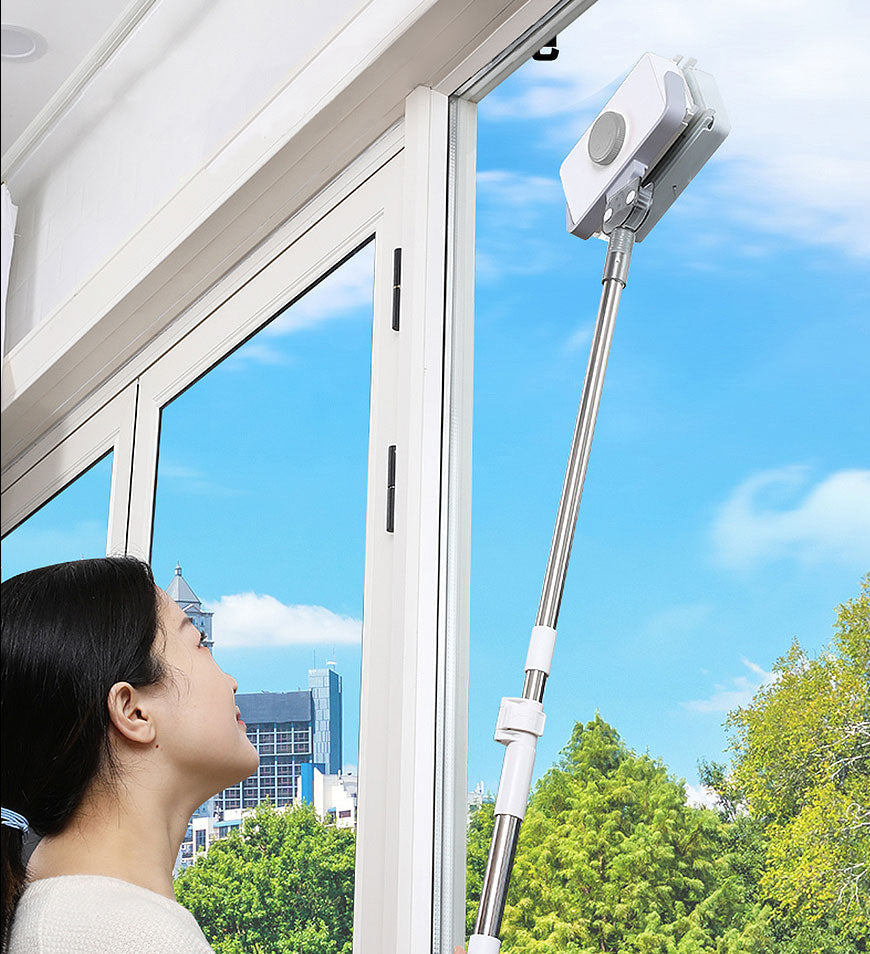 Fitlybuy magnetic dual-sided window cleaner with a long telescopic handle, being used by a woman to clean a high window.