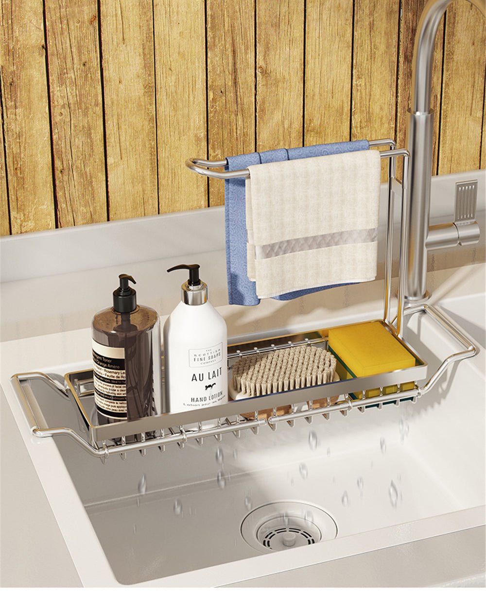 Adjustable stainless steel sink caddy holding soap bottles, a sponge, and a dish cloth over a white kitchen sink.