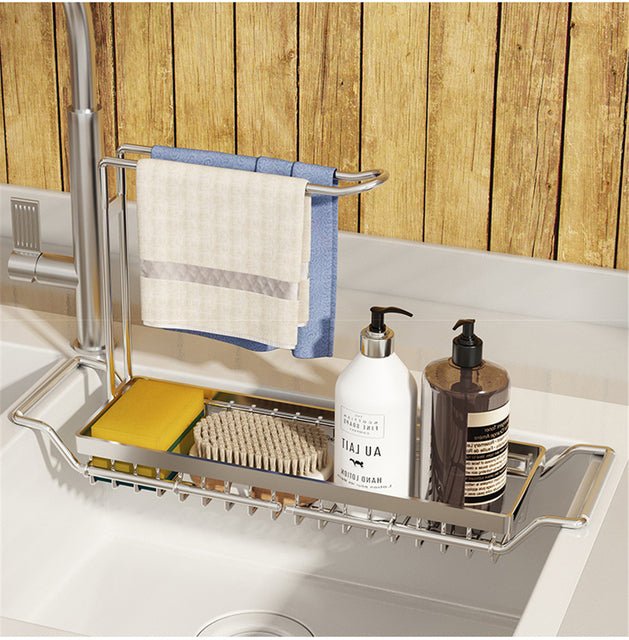 Silver adjustable over-sink organizer rack holding sponges, a brush, and soap bottles with a hanging kitchen towel.