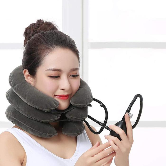 Woman wearing a grey, inflatable Fitlybuy cervical neck traction device and holding a hand-operated air pump.