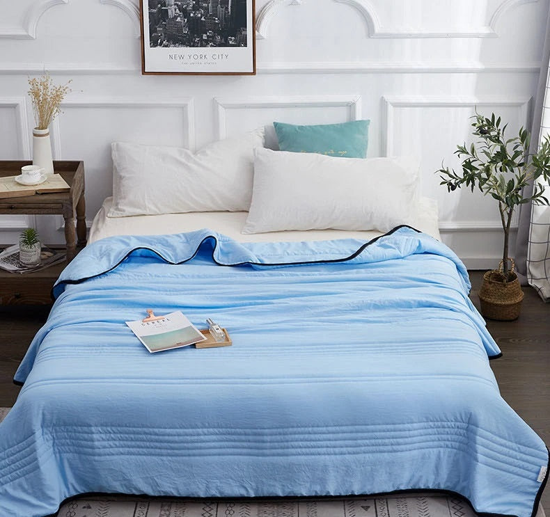 Light blue Fitlybuy cooling blanket with dark trim, neatly spread on a bed in a bright, modern bedroom setting.
