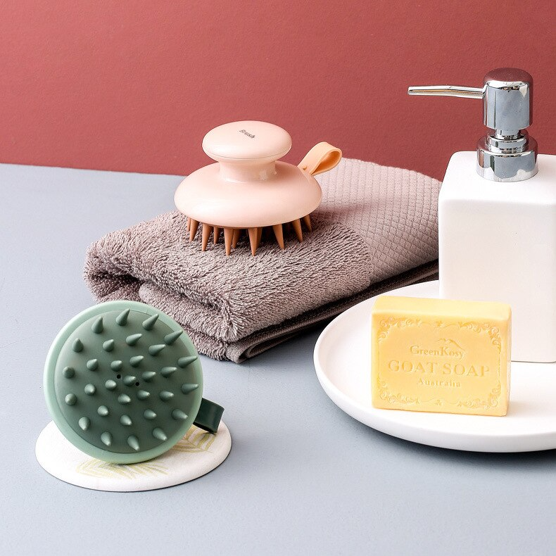 Fitlybuy Scalp Bliss Pro massagers in pink and green with ergonomic handles, resting on a towel next to bar soap.