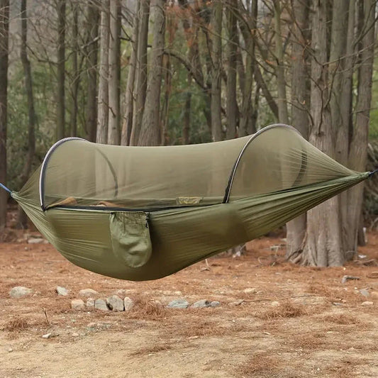 Olive green camping hammock with integrated BugShield mosquito net, hanging between forest trees.