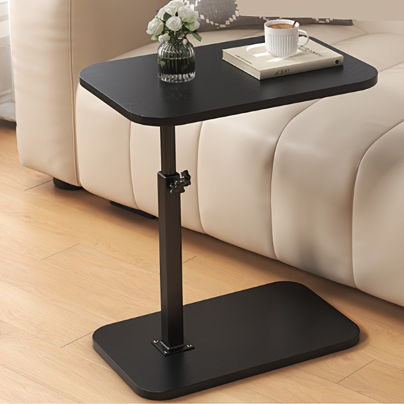 Black adjustable side table by a beige sofa, featuring a height-adjustment knob, holding a book, cup, and vase.
