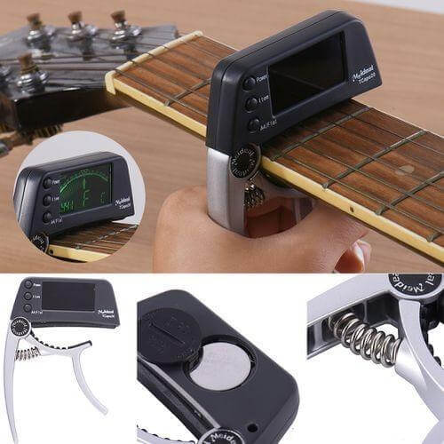 Black and silver 2-in-1 digital guitar tuner and capo attached to a guitar neck, showing display and battery detail.