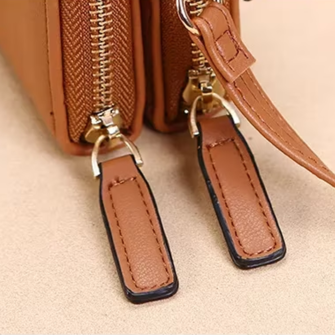 Close-up of a tan Fitlybuy leather crossbody bag featuring gold-tone zippers and stitched leather pull tabs.