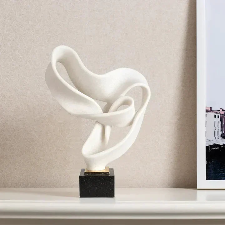 White abstract resin sculpture with flowing curves on a black square base, displayed on a shelf for modern home decor.