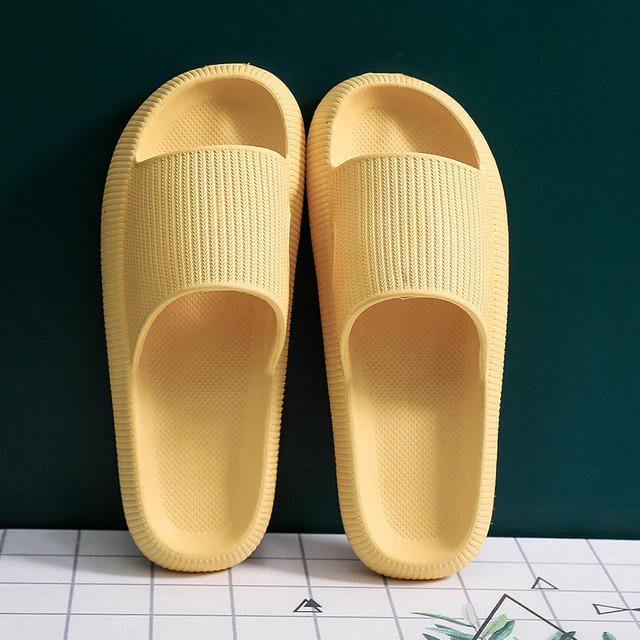 Pair of light yellow, textured rubber slide sandals with thick soles, positioned on a white grid surface.
