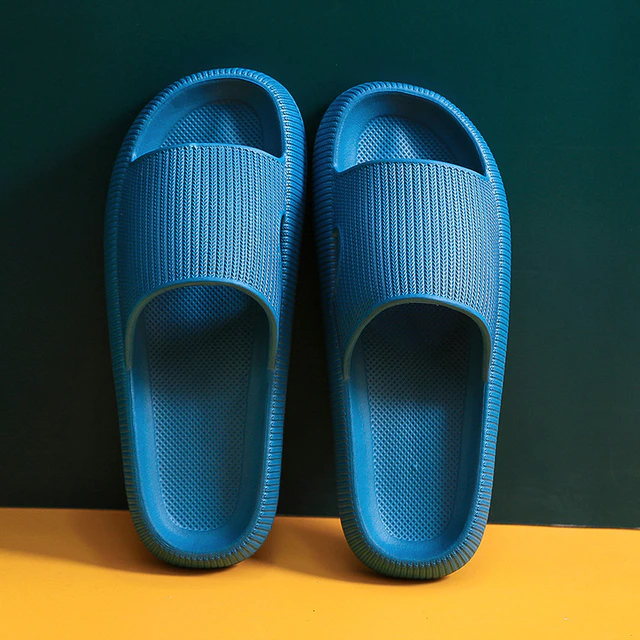 Pair of blue textured slide sandals on a yellow and dark green background. Fitlybuy exchange service image.